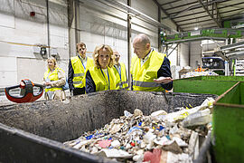 Vor einer Besuchergruppe zeigt ein Mann einer Frau eine Tonne mit Plastikmüll