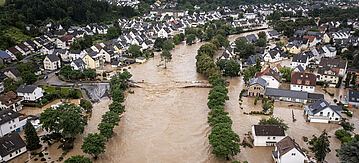 Blick auf einen übergetretenen Fluss und eine überschwemmte Stadt in einem Tal