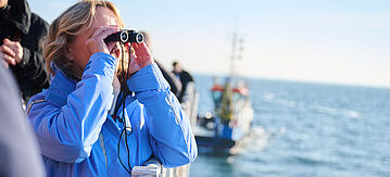 Steffi Lemke mit einem Fernglas auf einem Schiff. 