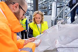 Ein Mann in einer orangefarbenen Jacke zeigt einer Frau in einer neongelben Weste ein weißes Granulat